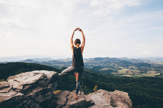Rear View Of Woman Practicing Yoga On Rock At Mountain Against Sky